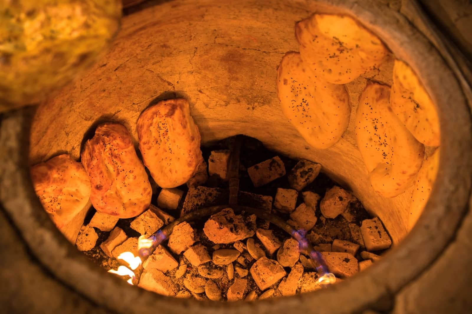 Stamped round breads baking on the inner wall of a tandoor above embers