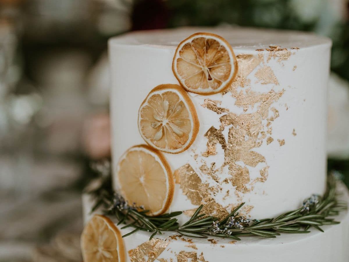 Tiered wedding cake with gold leaf, dried orange slices and rosemary