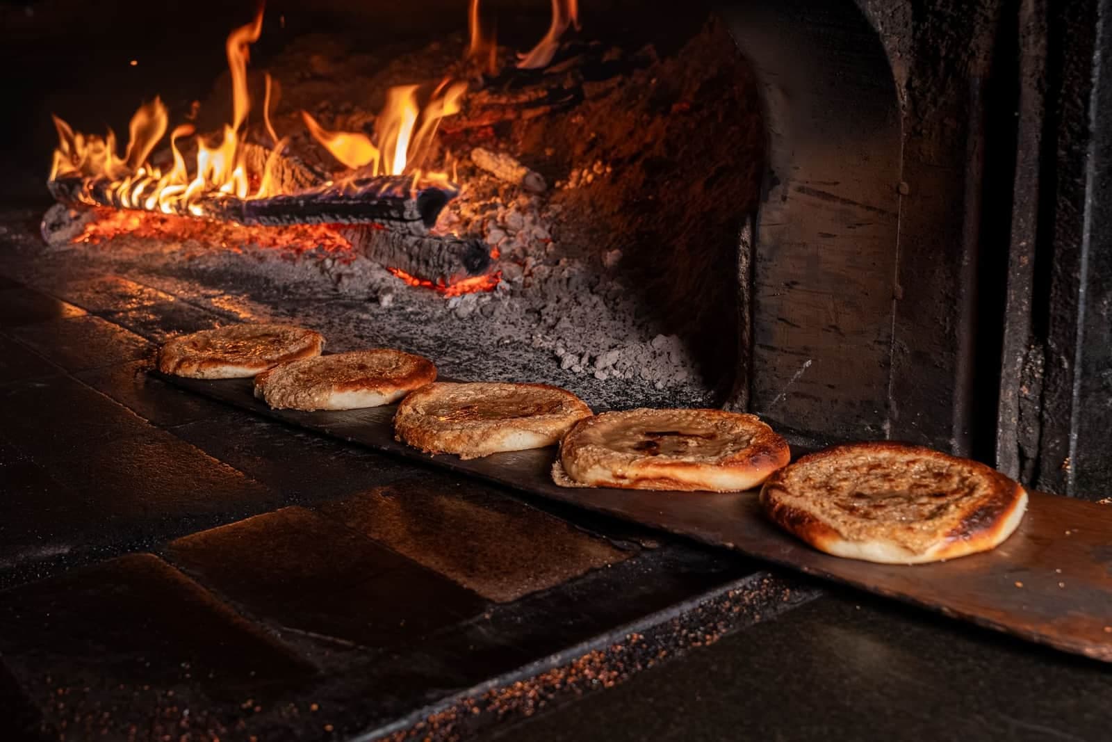 Glazed round breads on a wooden peel before a wood fire