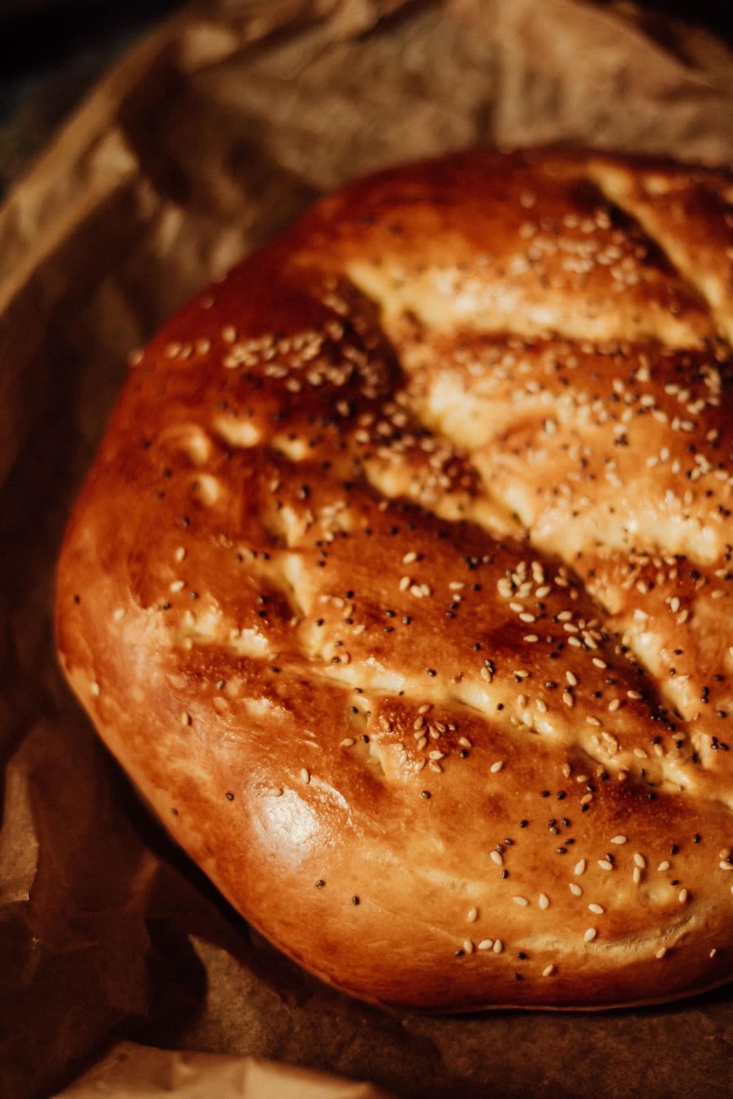 Round golden loaf scattered with sesame and nigella on kraft paper