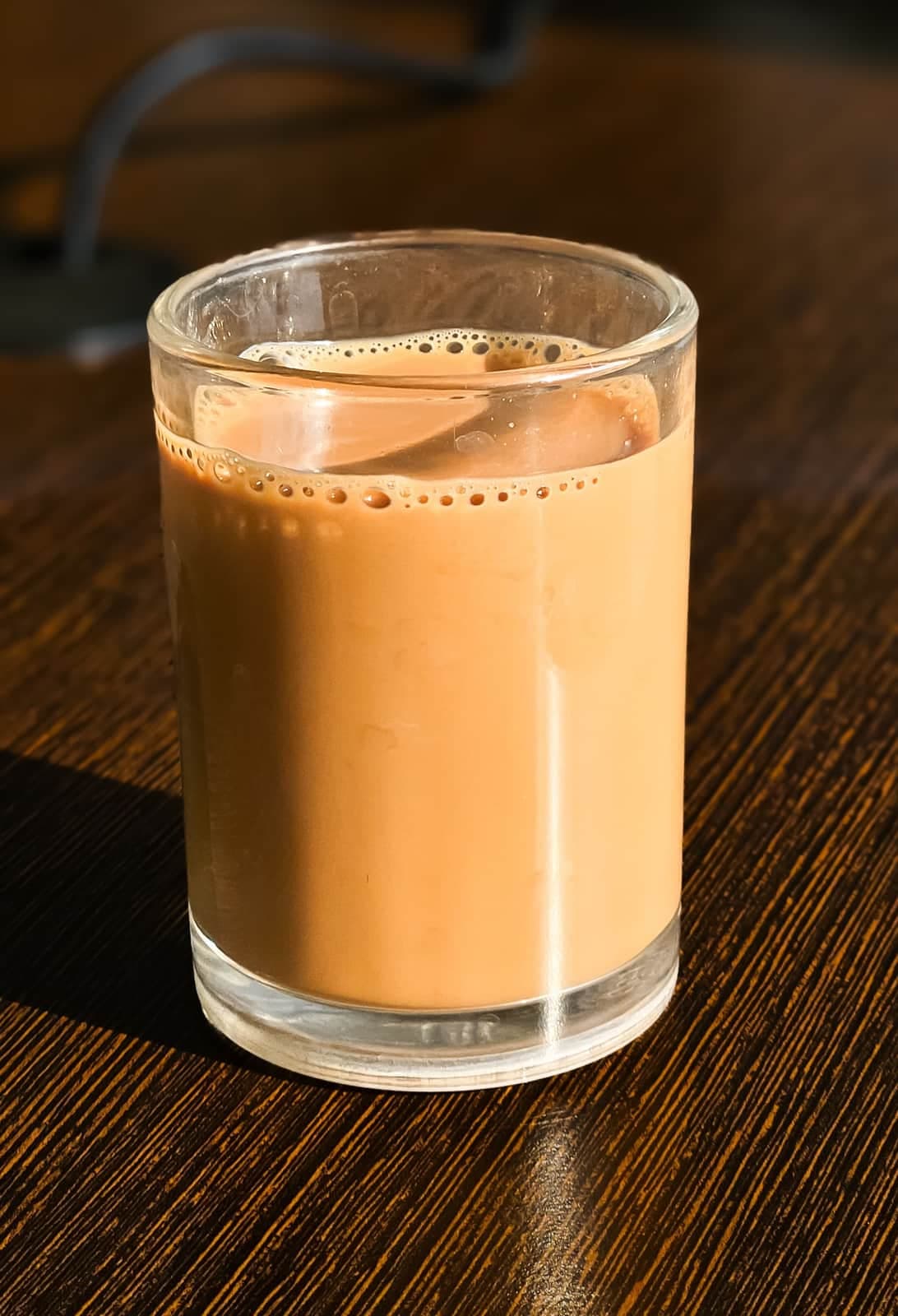 Glass of milky chai on a dark wooden table in morning sun