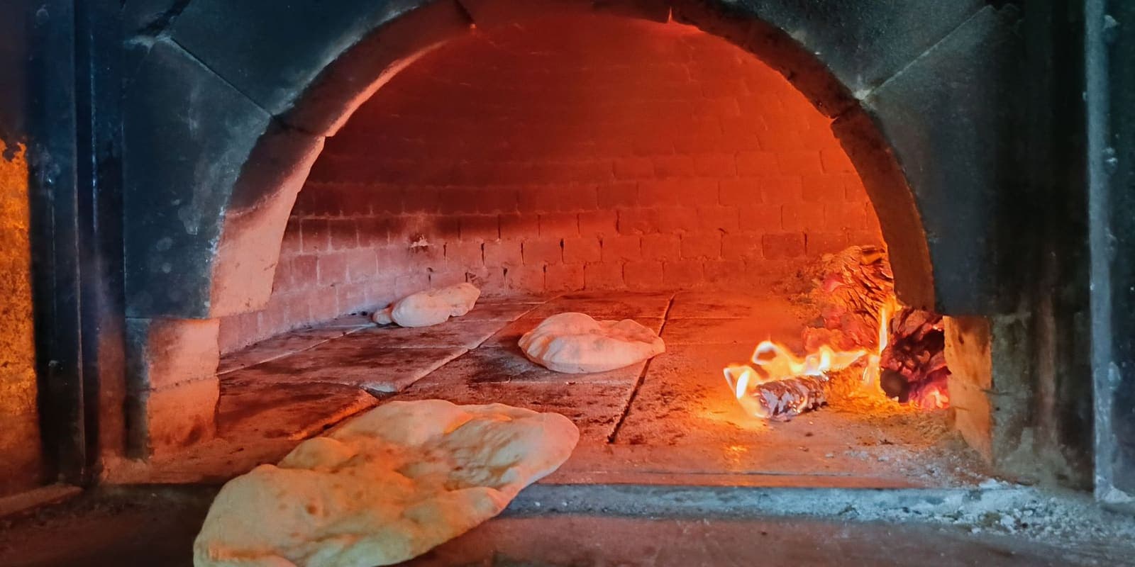 Flatbreads baking on the floor of a glowing wood-fired oven